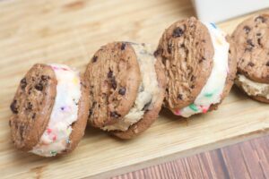 Shot of four edible cookie dough sandwiches laid on a wooden board.